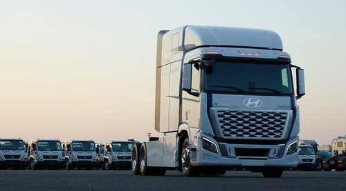 Front view of a Hyundai XCIENT Fuel Cell semi-truck parked on a lot at dusk, with a fleet of similar Hyundai trucks lined up in the background under a clear sky