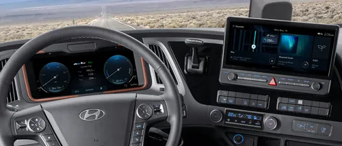 Interior view of the Hyundai XCIENT Fuel Cell truck showing the steering wheel, digital instrument cluster displaying trip data, and a center touchscreen with navigation, media, and hydrogen fuel information.